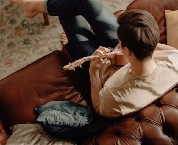 young man playing small guitare on a leather sofa